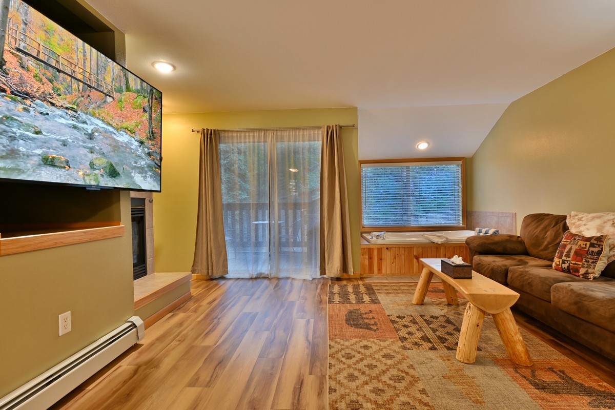 Condo living room in Riverview Suite with large smart TV, sofa, and jetted tub